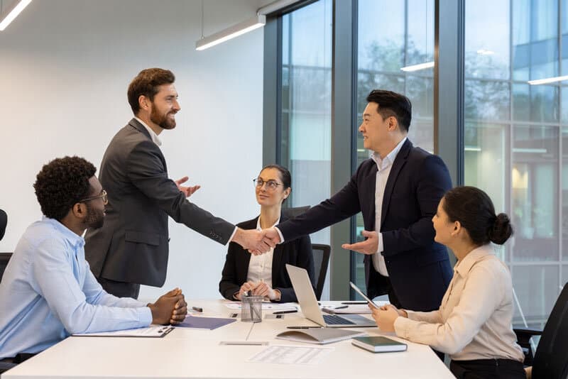 Two professionals shaking hands over documents during a due diligence meeting