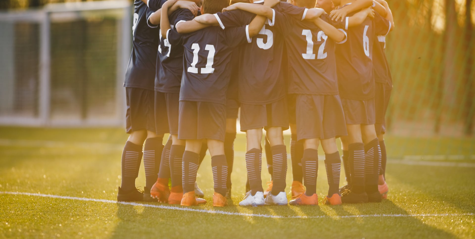 Group of children huddling with coach. Summer sunset at the stadium in the background. Youth soccer football team group photo. Happy boys soccer players kicking tournament. School