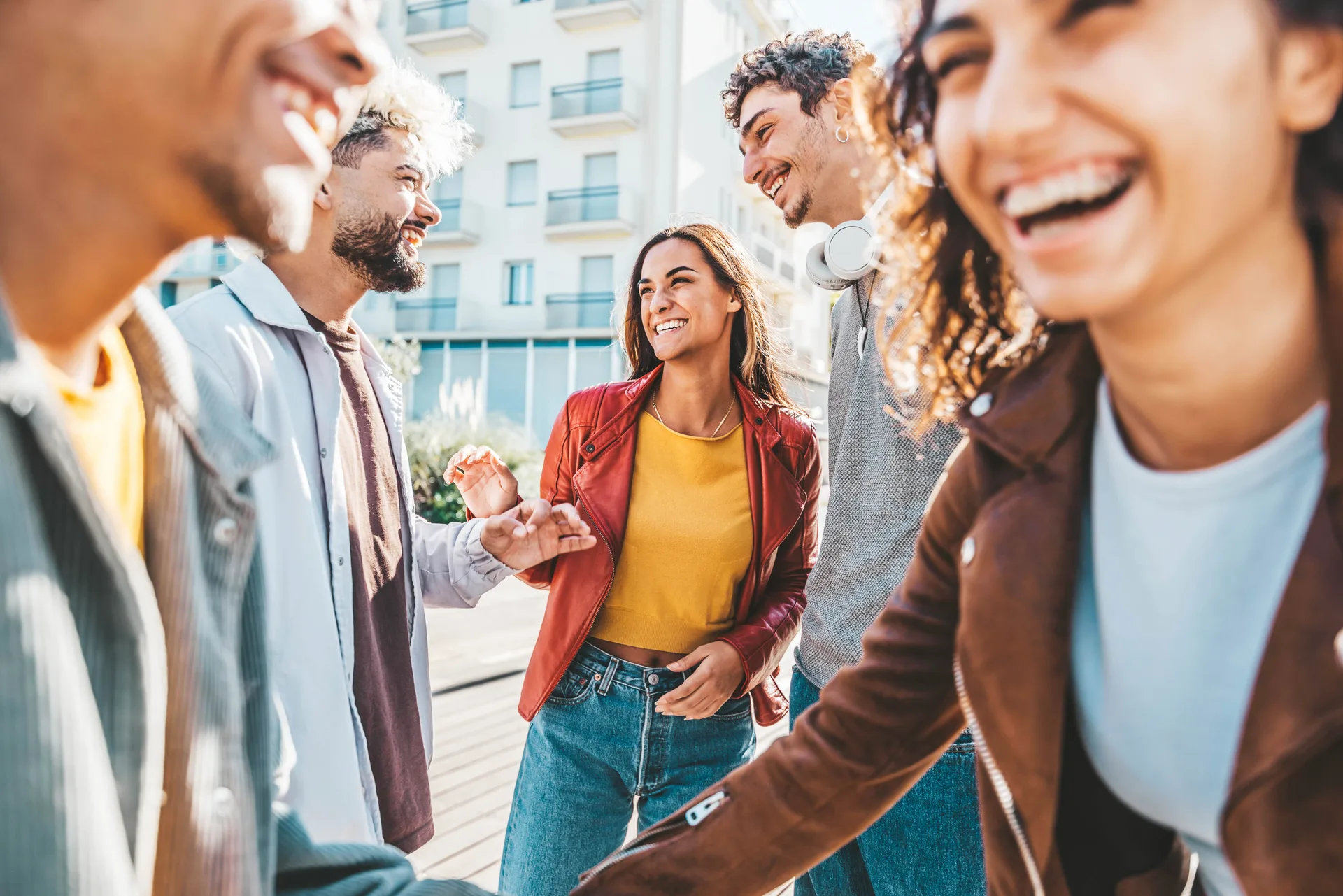 Happy multiracial friends having fun together walking on city street - Group of young people hanging out in town on a sunny day - University students talking and laugh out loud in
