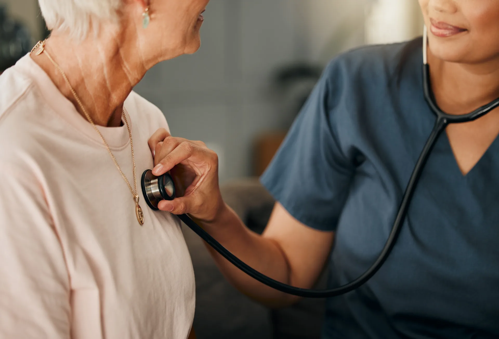 Cardiology consultation, doctor and senior woman consulting about healthcare on living room sofa in retirement home. Hand of nurse with stethoscope while helping elderly patient wi