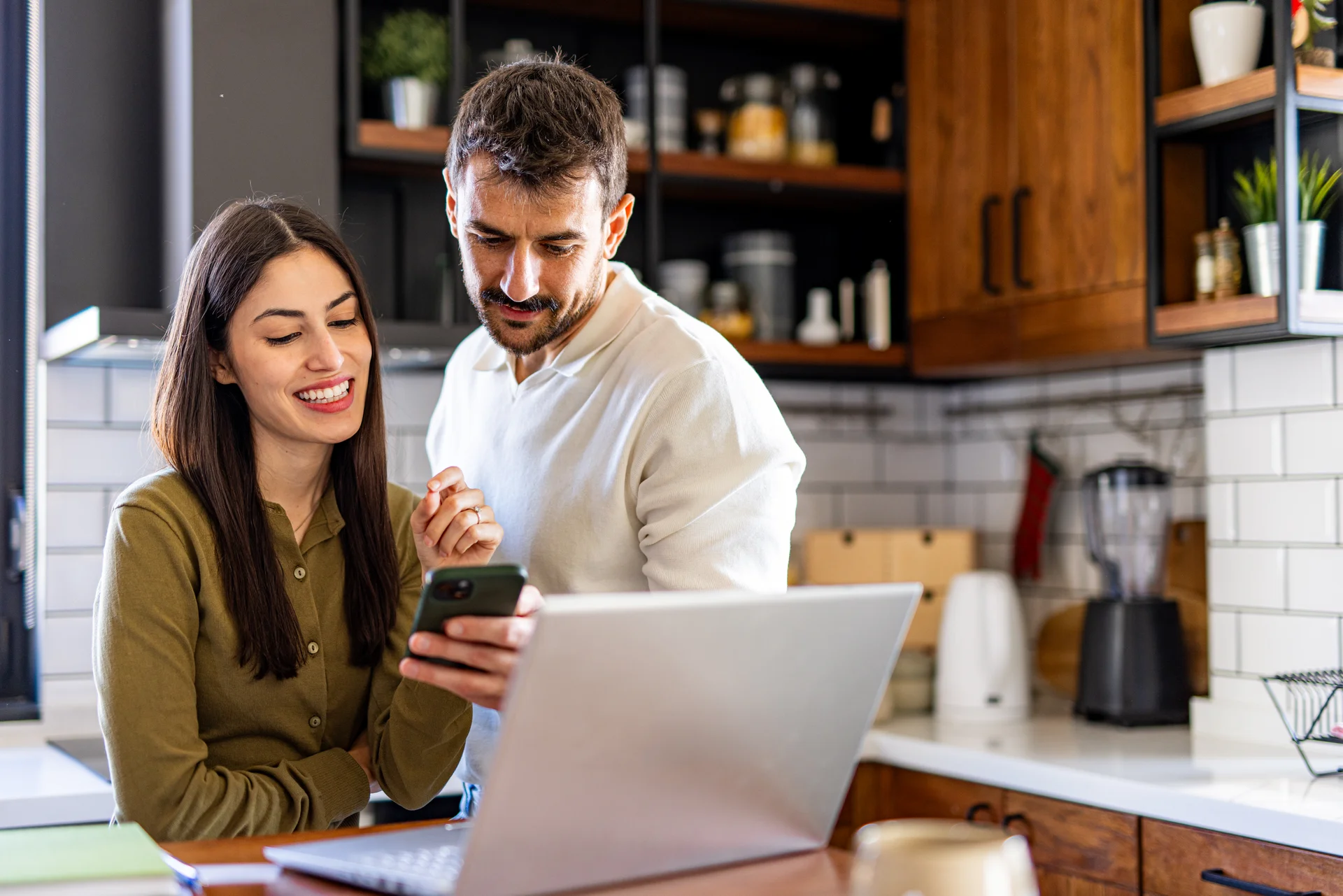 Couple using laptop and smartphone, checking their home finances in the kitchen