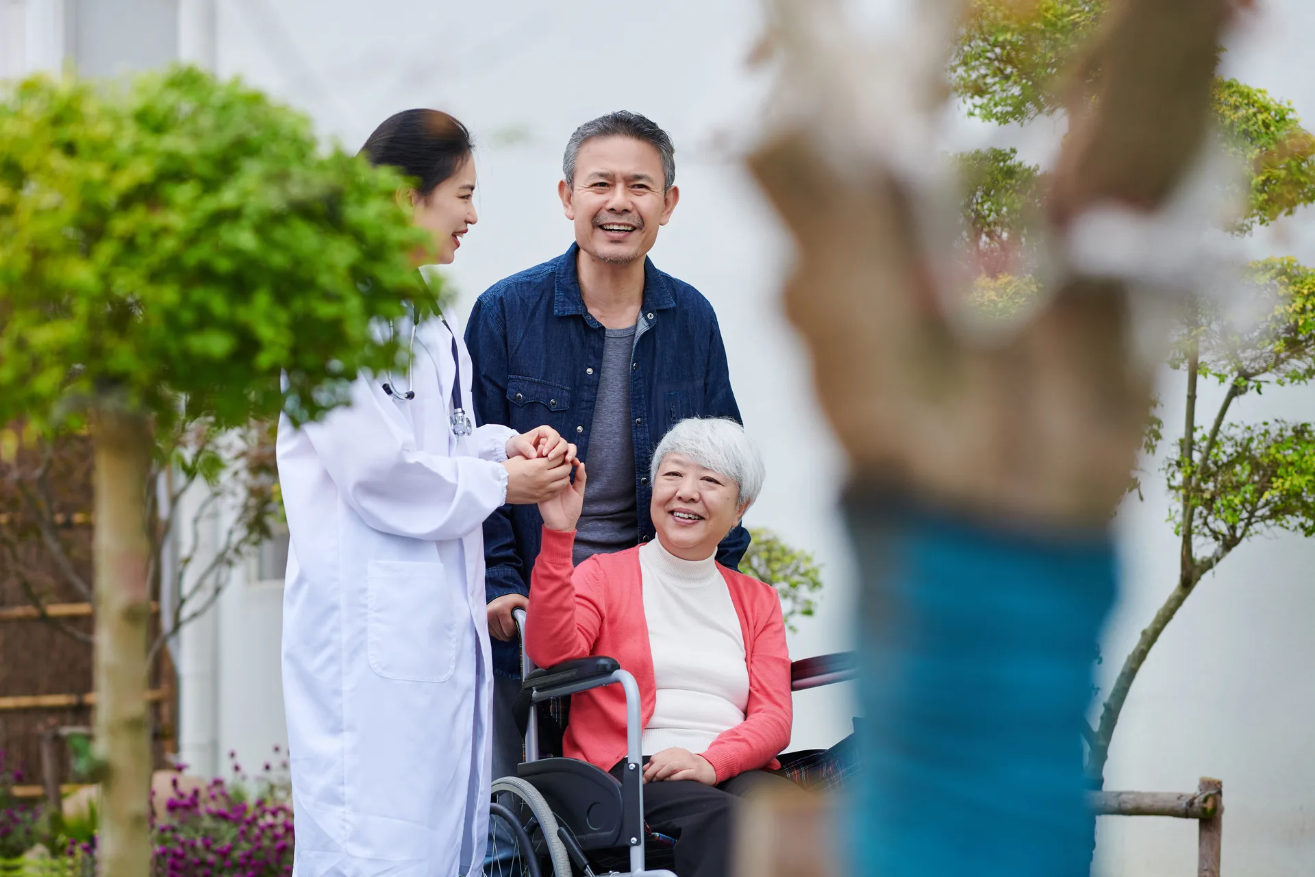 Female Doctor Accompany Senior Couple Walking while Talking outside Nursing Home's Garden